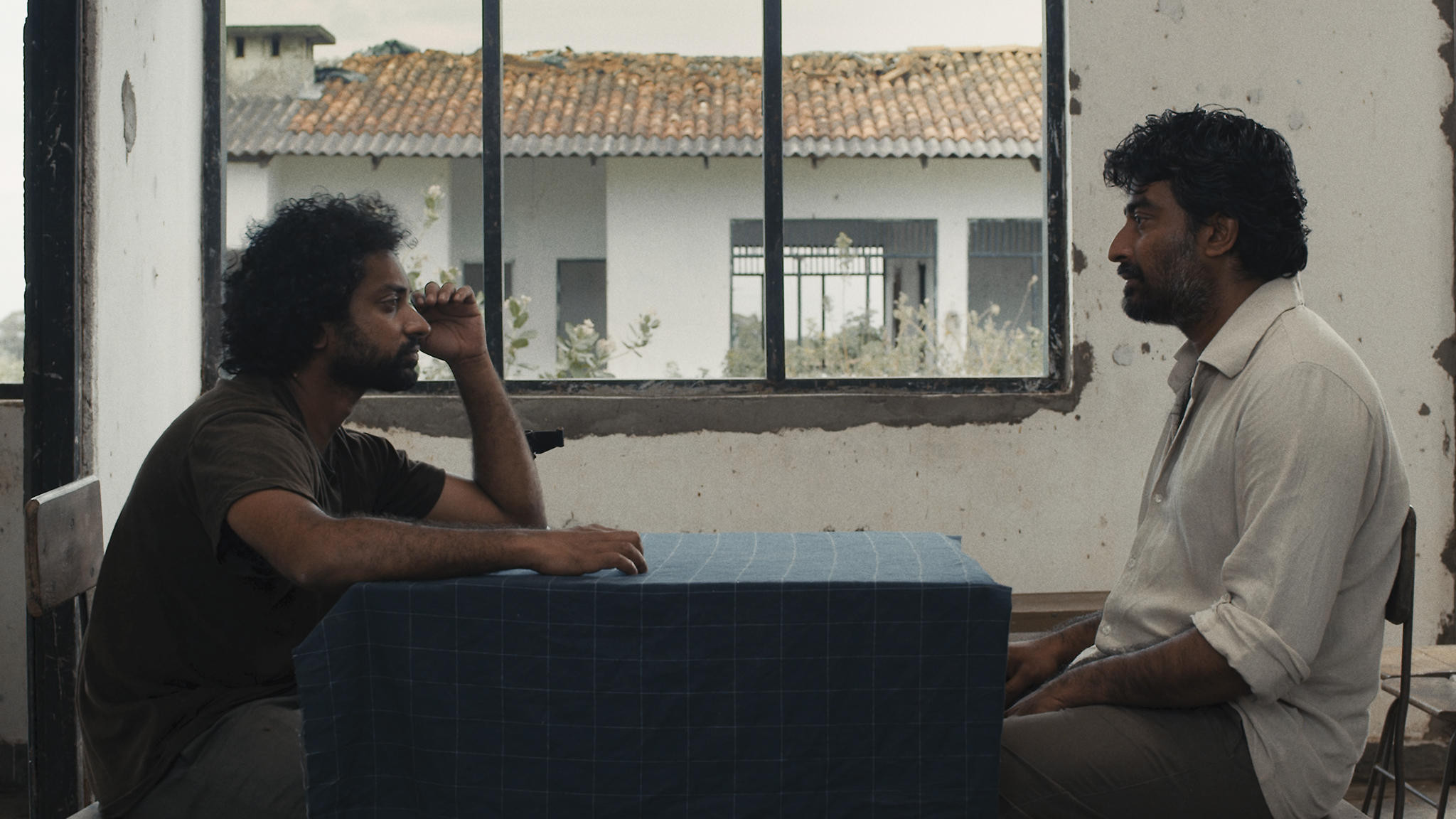 Two men in conversation at a table in a weathered Sri Lankan building
